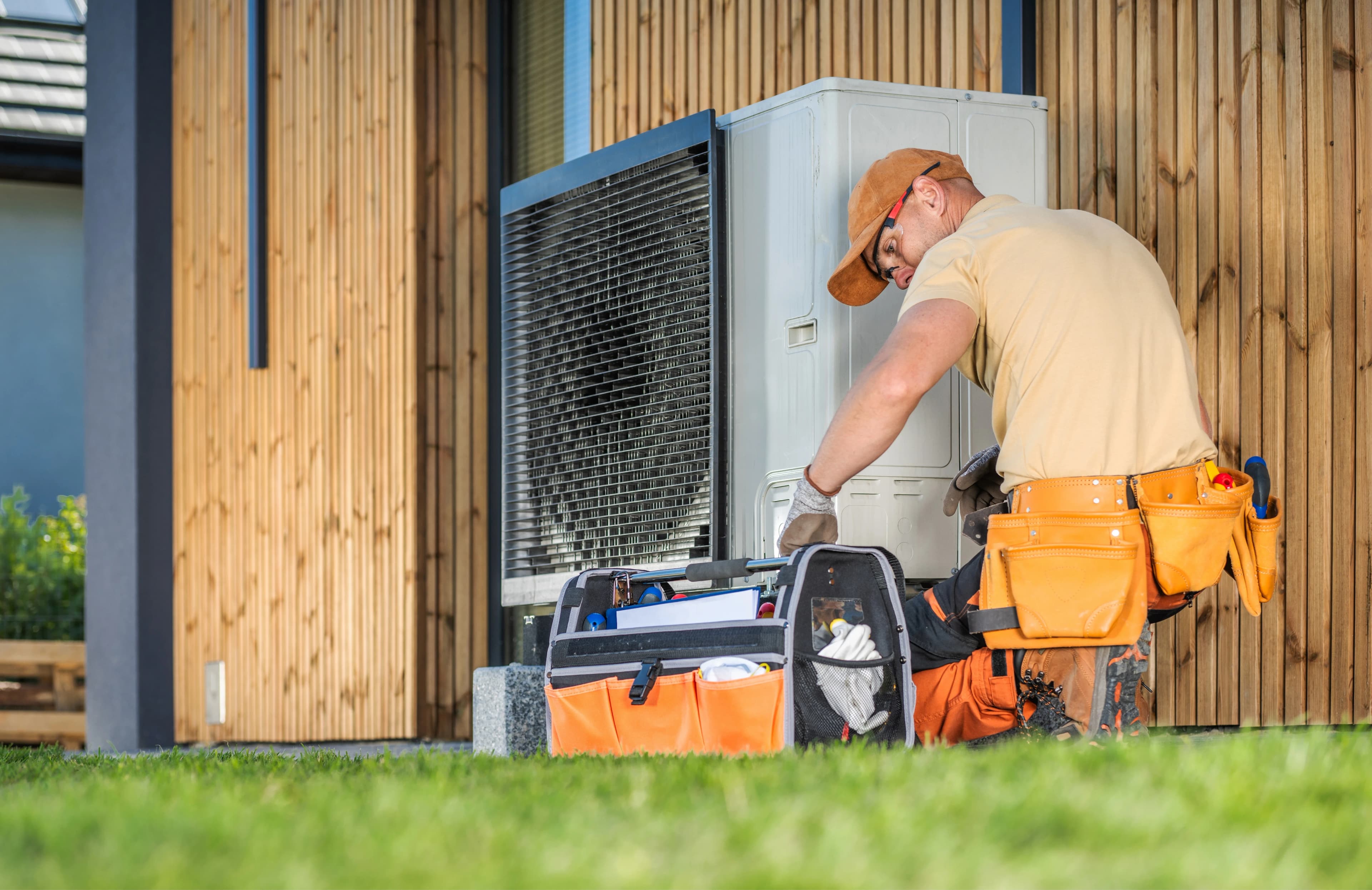 A HVAC technician is fixing a heat pump unit in the backyard of a house.